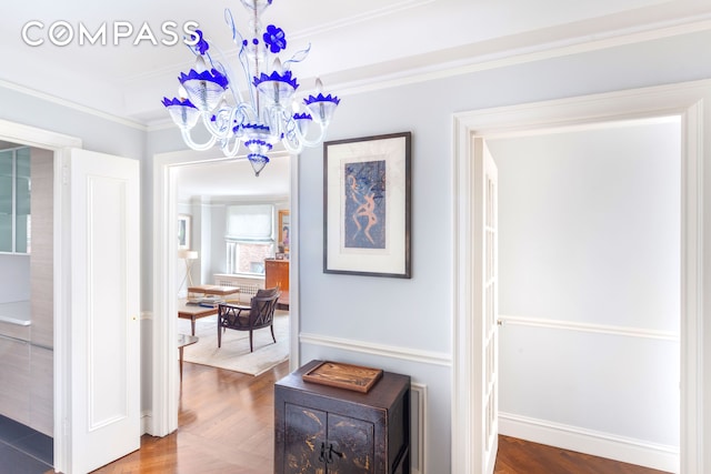 hallway with baseboards, crown molding, an inviting chandelier, and wood finished floors