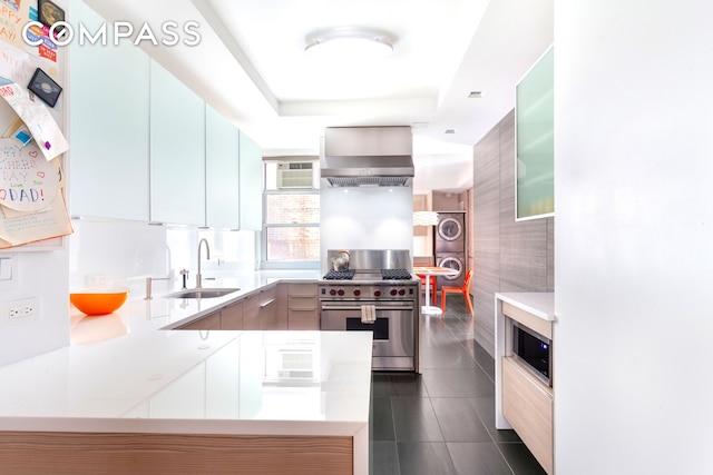 kitchen featuring appliances with stainless steel finishes, stacked washing machine and dryer, a sink, wall chimney range hood, and modern cabinets