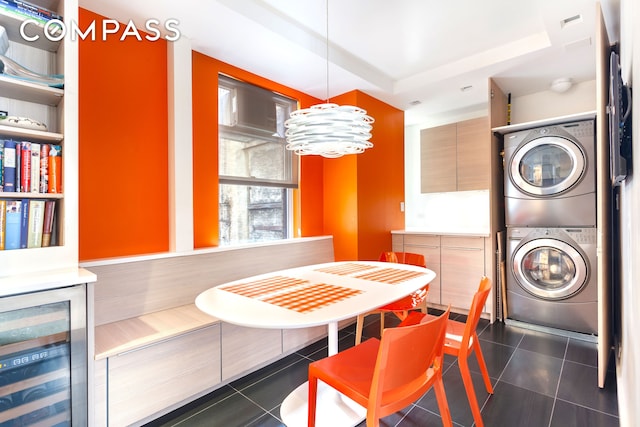 dining area with dark tile patterned floors, beverage cooler, a tray ceiling, and stacked washer / dryer