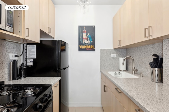 kitchen featuring stainless steel microwave, black gas range, decorative backsplash, light brown cabinetry, and a sink