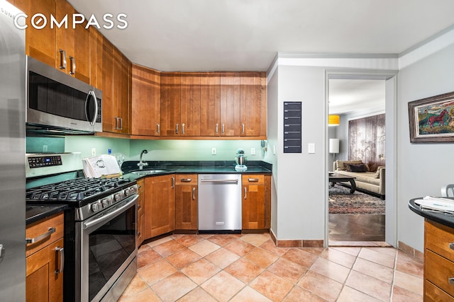 kitchen with dark countertops, brown cabinetry, stainless steel appliances, and a sink