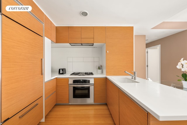 kitchen featuring a peninsula, gas stovetop, a sink, stainless steel oven, and light countertops