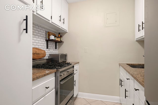 kitchen with light tile patterned floors, white cabinets, baseboards, backsplash, and stainless steel range with gas cooktop