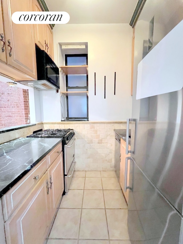 kitchen with light brown cabinets, tile walls, a wainscoted wall, light tile patterned floors, and stainless steel appliances