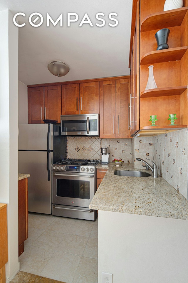 kitchen featuring a sink, backsplash, brown cabinetry, stainless steel appliances, and open shelves