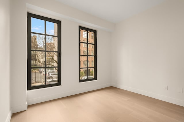 spare room featuring light wood-type flooring, plenty of natural light, and baseboards