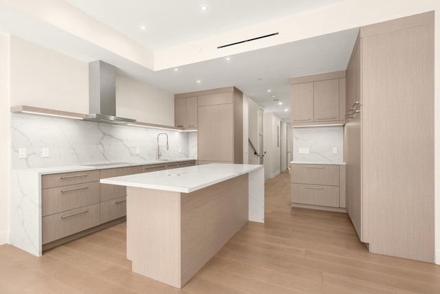 kitchen with wall chimney range hood, light wood-style flooring, modern cabinets, and backsplash