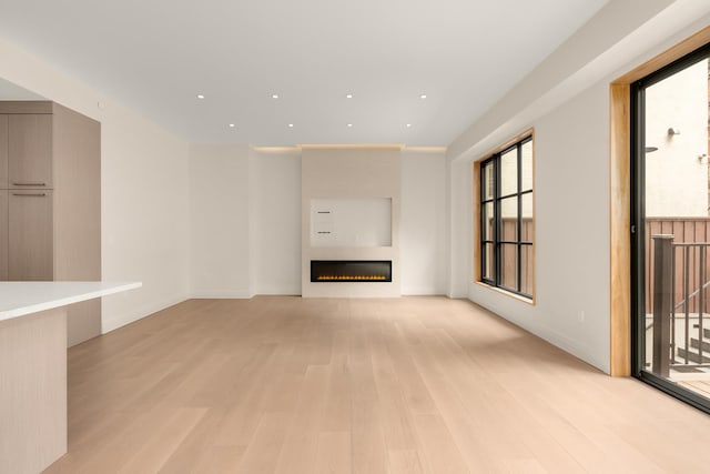 unfurnished living room with baseboards, light wood finished floors, a glass covered fireplace, and recessed lighting