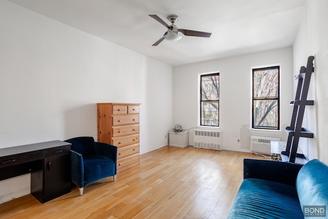 living area with a wall unit AC, a ceiling fan, baseboards, light wood finished floors, and radiator heating unit