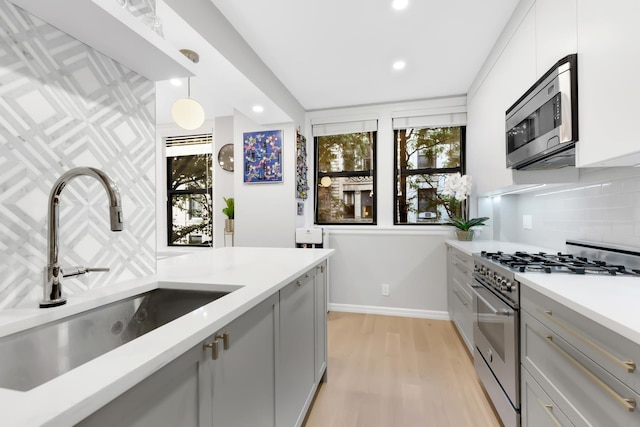 kitchen featuring stainless steel appliances, gray cabinets, backsplash, light wood-style flooring, and a sink