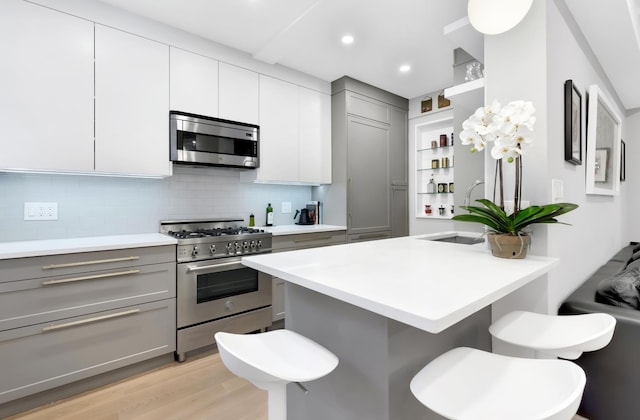 kitchen with open shelves, a kitchen breakfast bar, stainless steel appliances, and gray cabinetry