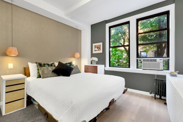 bedroom with cooling unit, radiator, baseboards, and wood finished floors