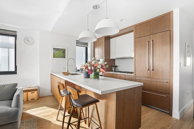 kitchen with light wood-type flooring, modern cabinets, a breakfast bar, a sink, and a peninsula