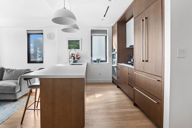 kitchen with a sink, light wood-style floors, open floor plan, light countertops, and a kitchen bar