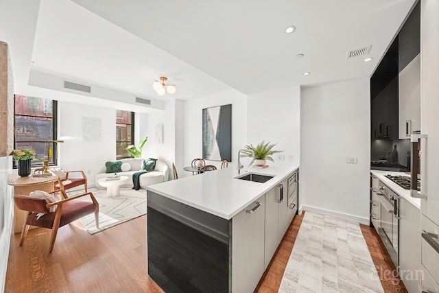 kitchen with light wood finished floors, visible vents, a sink, modern cabinets, and a peninsula