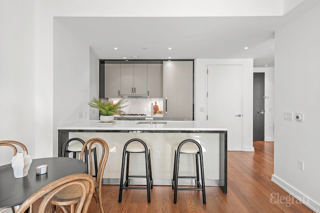 kitchen featuring wood finished floors, a peninsula, light countertops, gray cabinetry, and backsplash