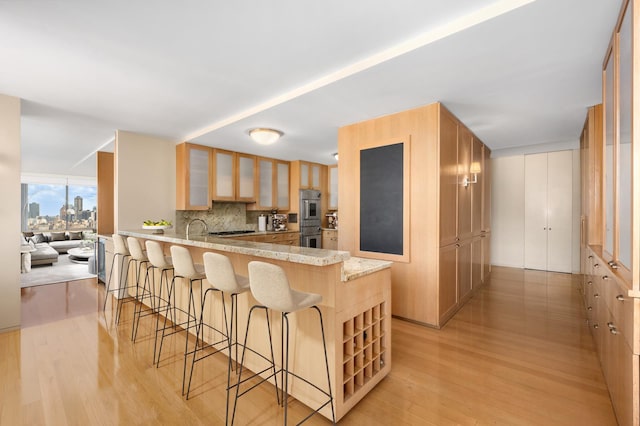 kitchen with glass insert cabinets, a kitchen breakfast bar, a peninsula, stainless steel double oven, and light wood-style floors