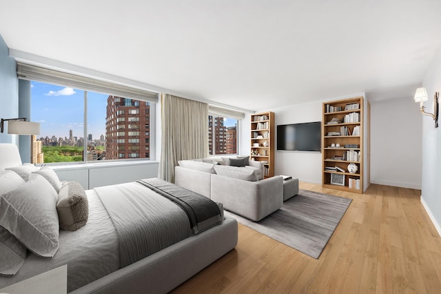 bedroom with light wood-style floors, multiple windows, baseboards, and a city view