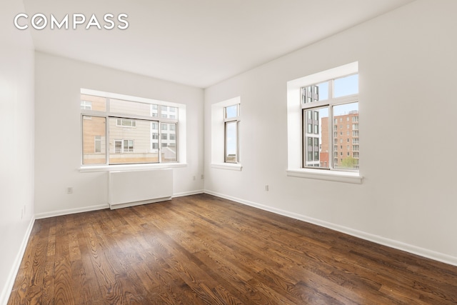 unfurnished room featuring a wealth of natural light, dark wood-style floors, baseboards, and radiator heating unit