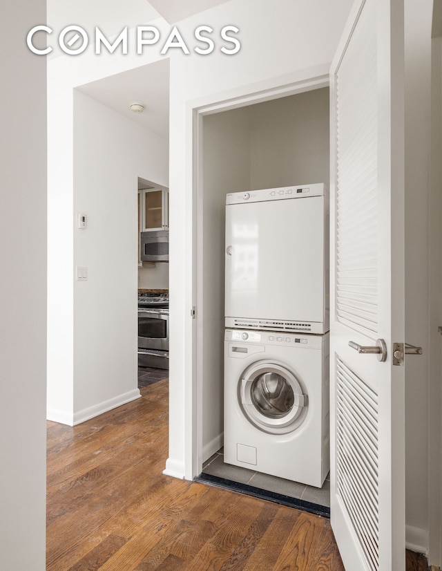 laundry room featuring baseboards, stacked washer and clothes dryer, wood finished floors, and laundry area
