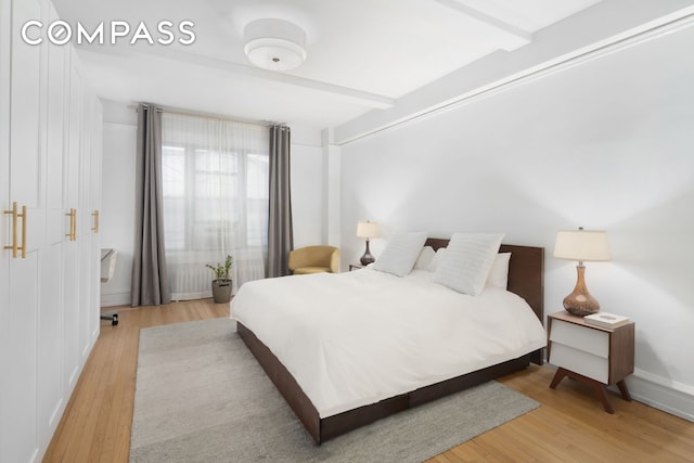 bedroom featuring beamed ceiling, baseboards, and wood finished floors