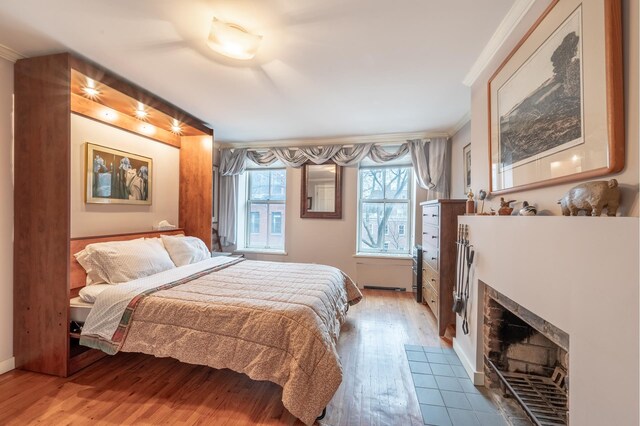 bedroom with a tiled fireplace, crown molding, and light wood finished floors