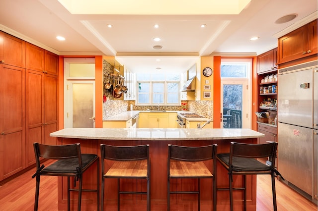 kitchen with light wood finished floors, light stone countertops, under cabinet range hood, high quality appliances, and a sink