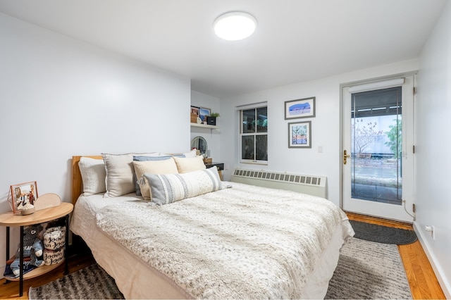 bedroom with wood finished floors, radiator heating unit, and access to outside