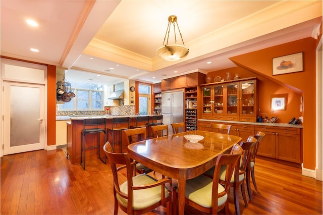 dining area with a raised ceiling, crown molding, recessed lighting, and wood-type flooring