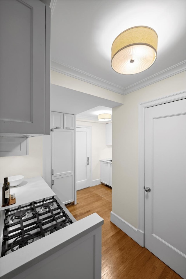 kitchen with light wood-style flooring, baseboards, light countertops, cooktop, and crown molding