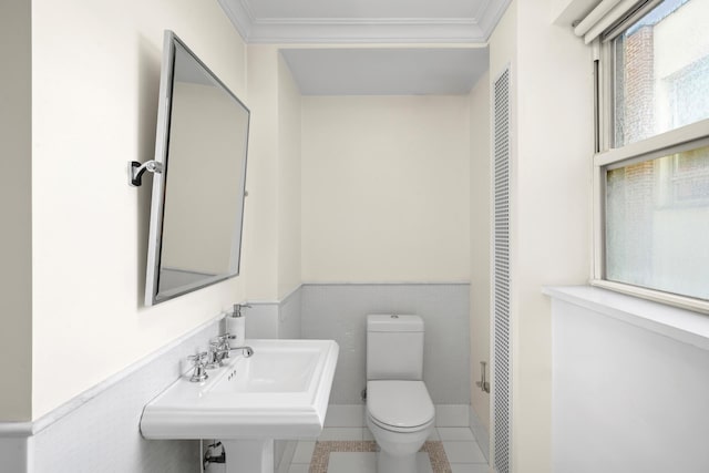 half bathroom with toilet, a wainscoted wall, a sink, ornamental molding, and tile patterned floors