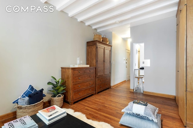 sitting room featuring lofted ceiling with beams, baseboards, and light wood finished floors