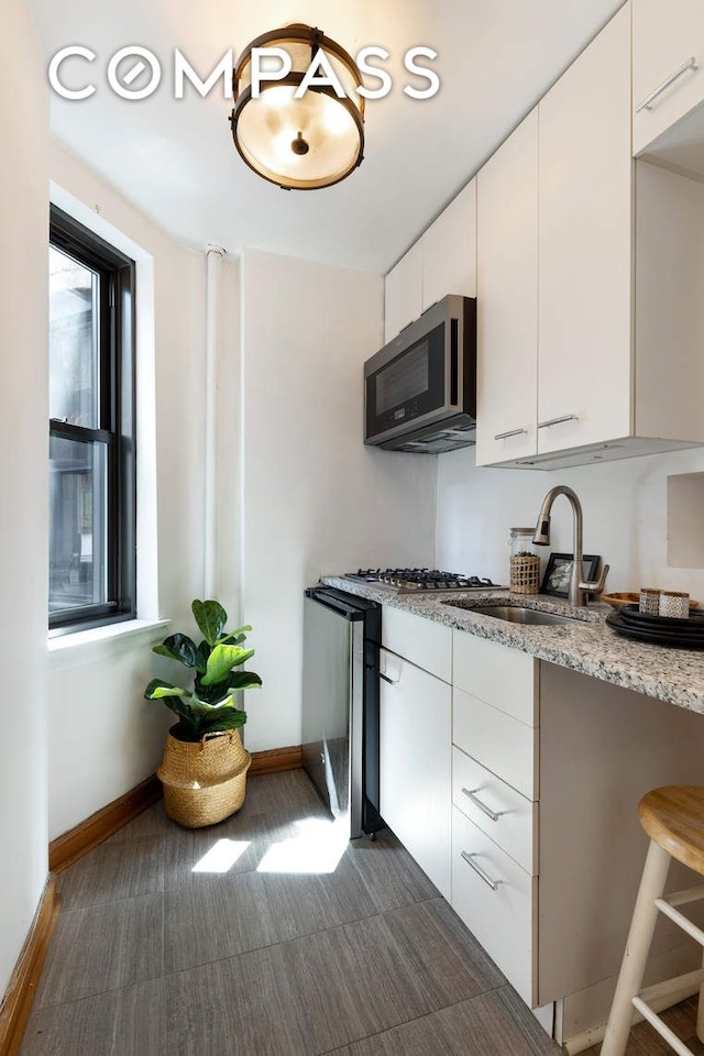 kitchen with baseboards, stainless steel microwave, a sink, and white cabinets