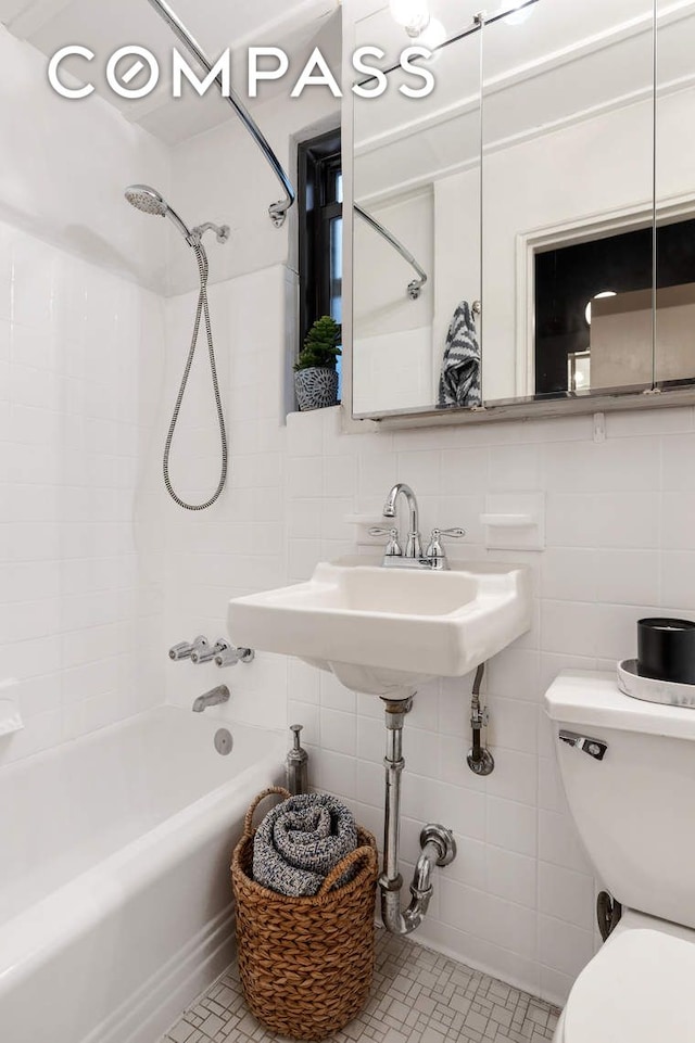 full bathroom with toilet, a sink, washtub / shower combination, and tile walls