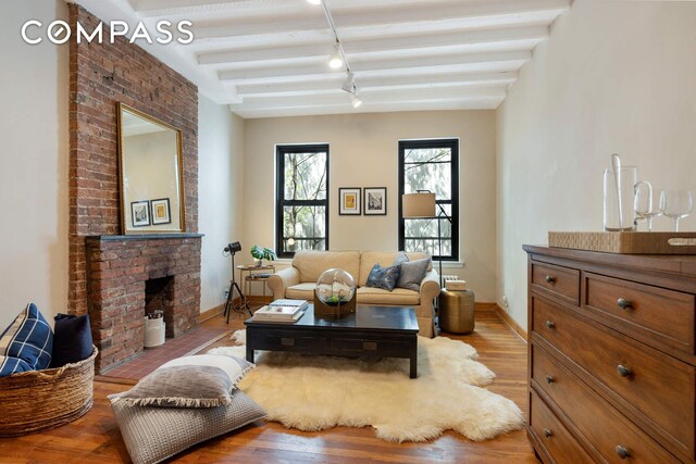 living room with a brick fireplace, light wood-style flooring, baseboards, and beam ceiling