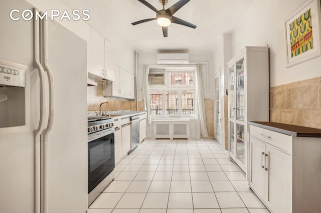 kitchen featuring light tile patterned floors, white cabinets, a wall unit AC, ceiling fan, and appliances with stainless steel finishes