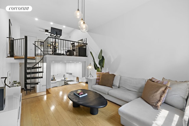 living room with recessed lighting, visible vents, light wood-style flooring, a towering ceiling, and stairs