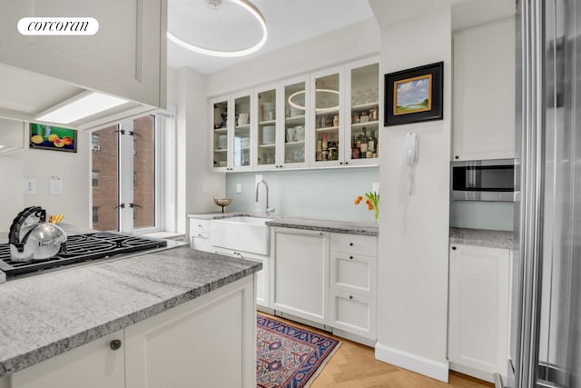 kitchen with light stone countertops, glass insert cabinets, white cabinetry, a sink, and stainless steel appliances