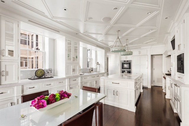 kitchen with black microwave, light countertops, an island with sink, and white cabinets