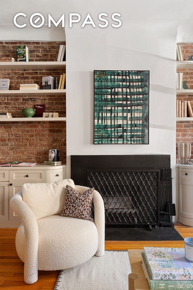 sitting room featuring a fireplace with flush hearth, brick wall, and wood finished floors