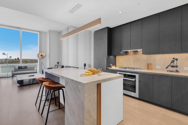 kitchen featuring a breakfast bar, light countertops, appliances with stainless steel finishes, dark cabinetry, and under cabinet range hood