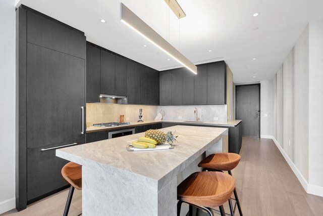 kitchen featuring paneled built in refrigerator, a kitchen breakfast bar, dark cabinets, and light countertops