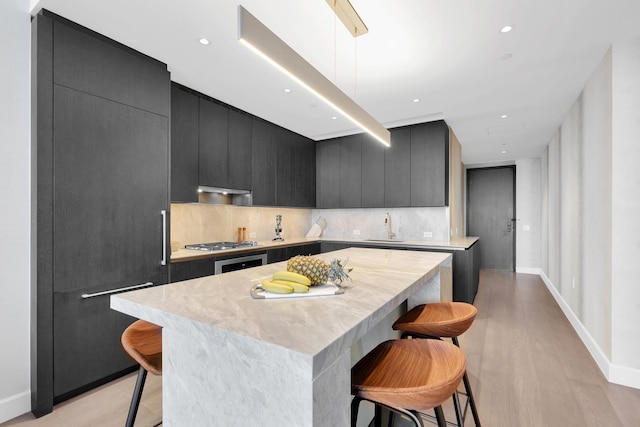 kitchen featuring dark cabinetry, a kitchen breakfast bar, a sink, and light countertops