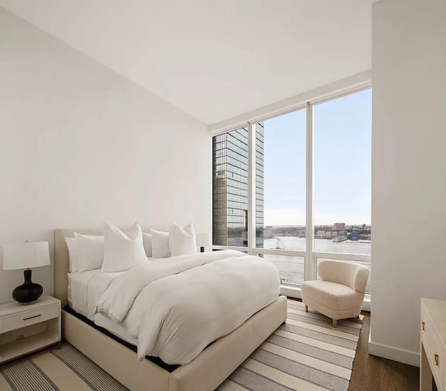 bedroom featuring a water view, baseboards, a wall of windows, and wood finished floors