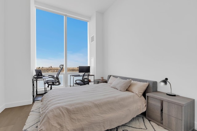 bedroom featuring baseboards, floor to ceiling windows, wood finished floors, and visible vents