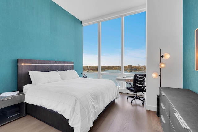 bedroom featuring a wall of windows, a water view, and wood finished floors