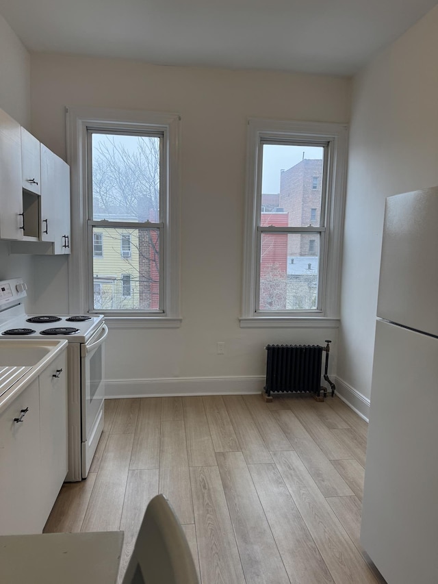 kitchen featuring white appliances, radiator, a healthy amount of sunlight, light wood-style floors, and white cabinetry