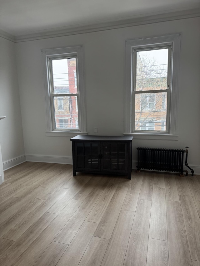 empty room featuring light wood-style flooring, radiator, baseboards, and ornamental molding