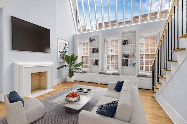 living room with a fireplace with flush hearth, light wood-style floors, baseboards, a towering ceiling, and stairs