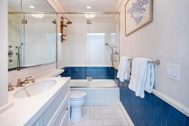 bathroom with bath / shower combo with glass door, toilet, tile patterned floors, vanity, and wainscoting